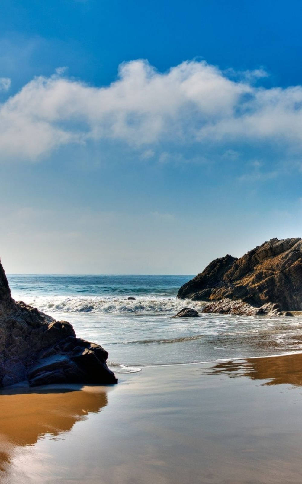 A Beach With Rocks And A Blue Sky Wallpaper