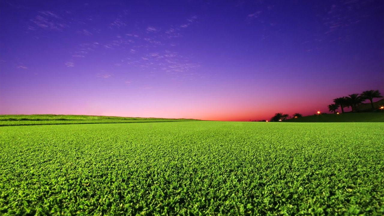 A Beautiful Sky Of Pink And Orange Hues Sets A Serene Backdrop For A Pristine Golf Course Lined With Lush Green Grass Wallpaper