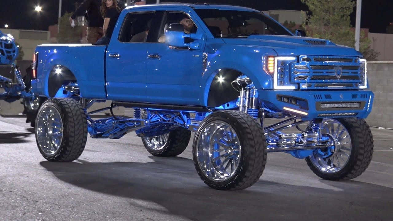 A Blue Truck With A Large Tire On It Wallpaper