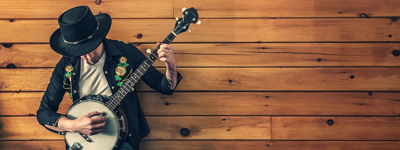 A Man In A Cowboy Hat Playing A Banjo Wallpaper