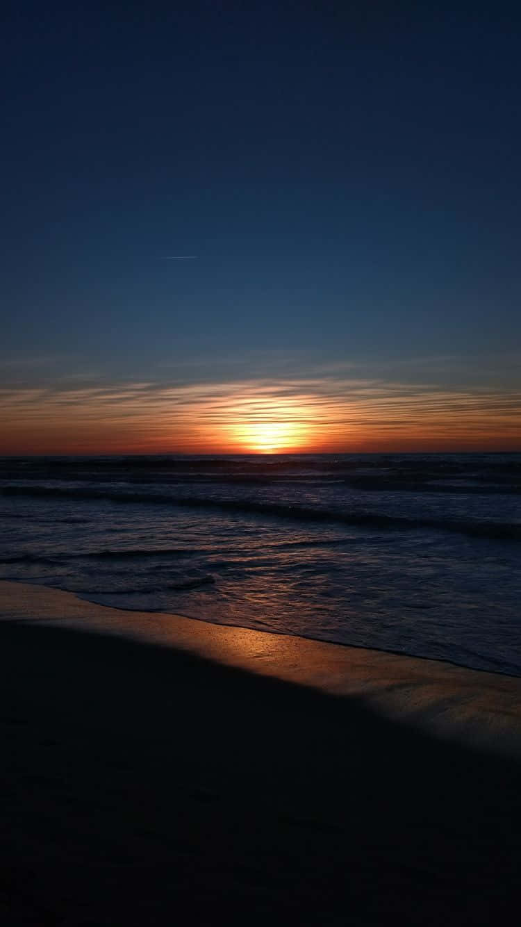 A Sunset Over The Ocean With A Sand Beach Wallpaper