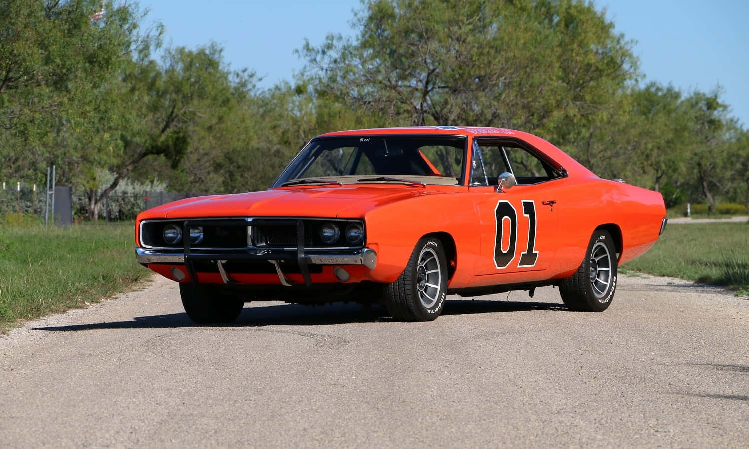 An Orange Car Is Driving Down A Road Wallpaper