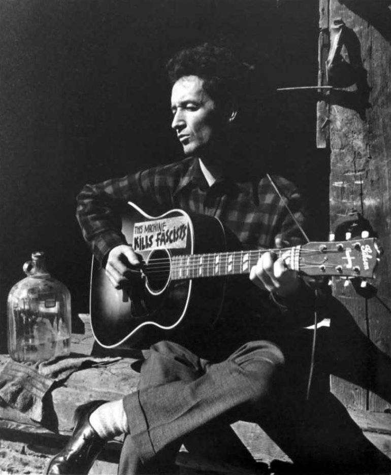 “folk Music Legend - Woody Guthrie Strumming His Guitar On A Bustling Street