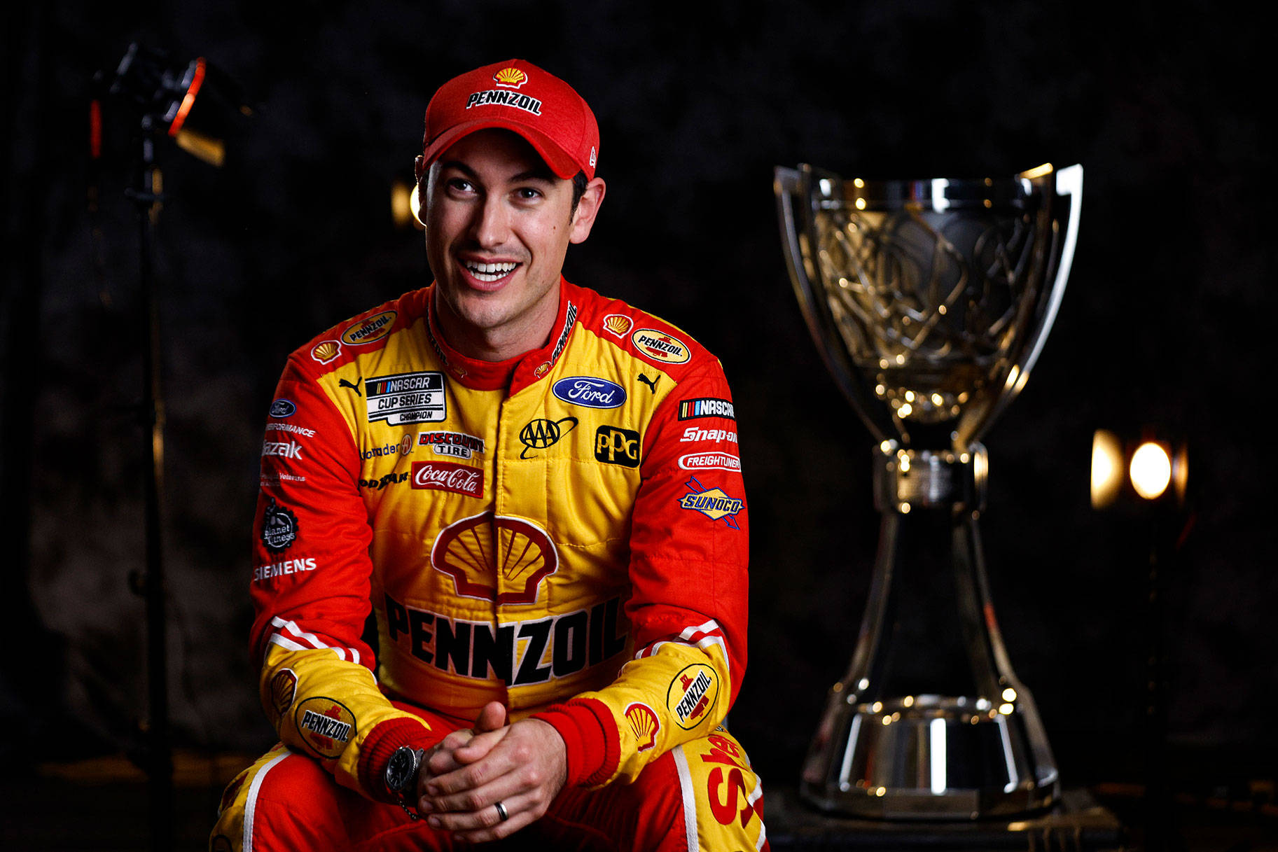 Joey Logano Sitting Beside Blurred Trophy Wallpaper