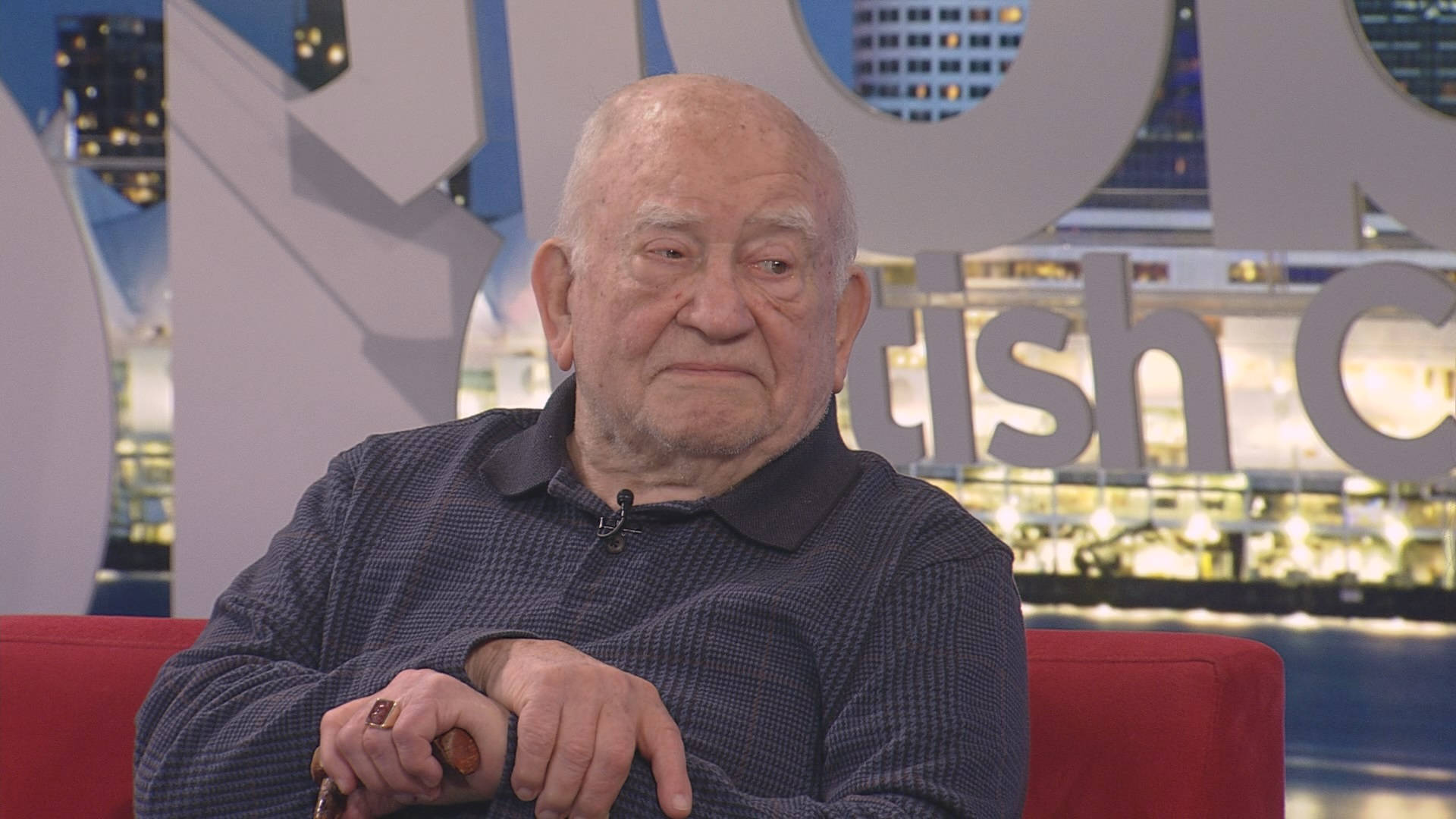 Legendary Actor Edward Asner Relaxing On A Red Couch Wallpaper