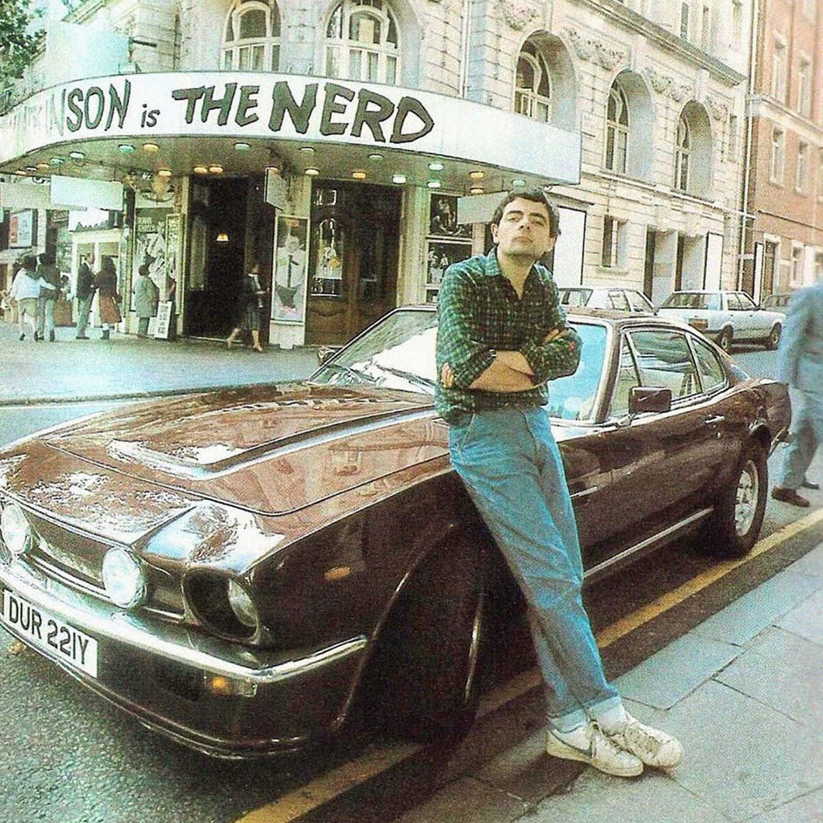 Rowan Atkinson Leaningon Car Outside Theatre Wallpaper