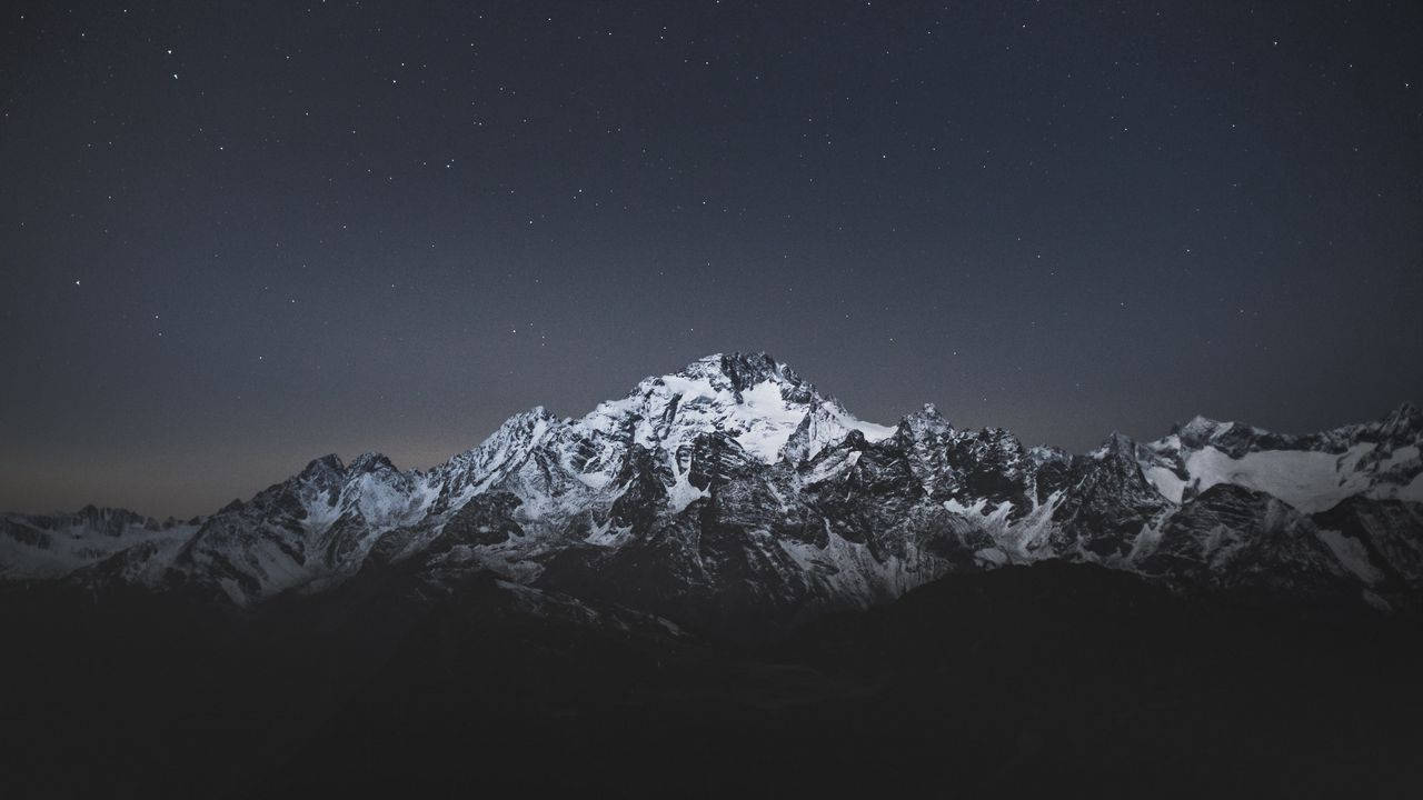 Stand Tall And Admire The Beauty Of The Night Sky And A Majestic Mountain. Wallpaper