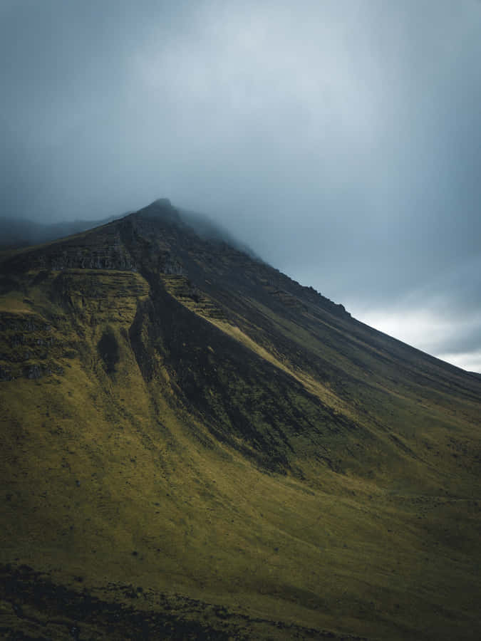 A Mountain Covered In Clouds With Grass And Grass Wallpaper