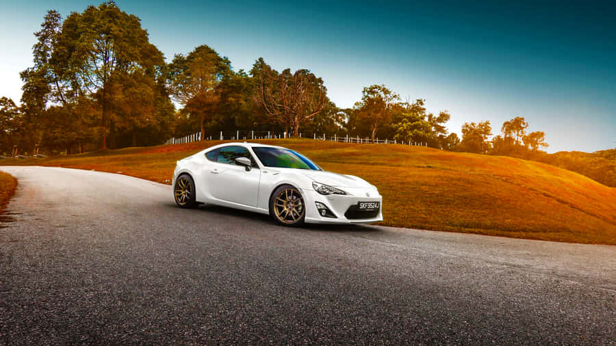 A White Sports Car Driving Down A Road Wallpaper