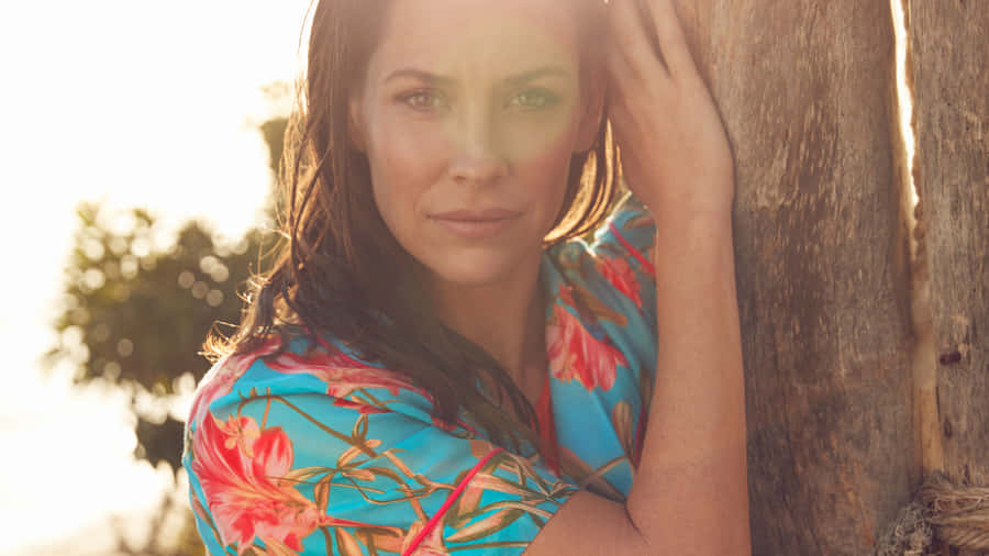 A Woman In A Floral Dress Leaning Against A Wooden Pole Wallpaper