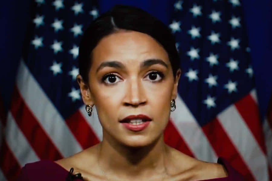 Alexandria Ocasio-cortez In Front Of American Flag Wallpaper