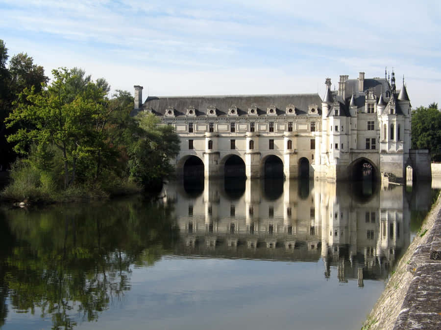 Breathtaking View Of Chenonceau Castle Amidst Riverside Vegetation Wallpaper