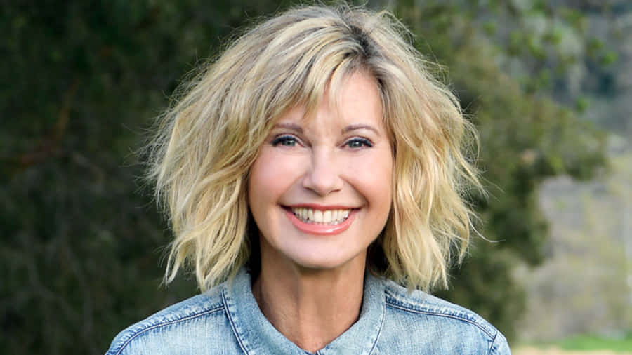 Olivia Newton John Against Blurry Green Trees Wallpaper