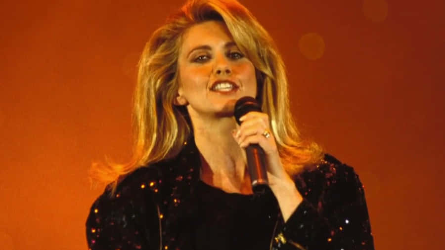 Olivia Newton John Singing In Orange Backdrop Wallpaper