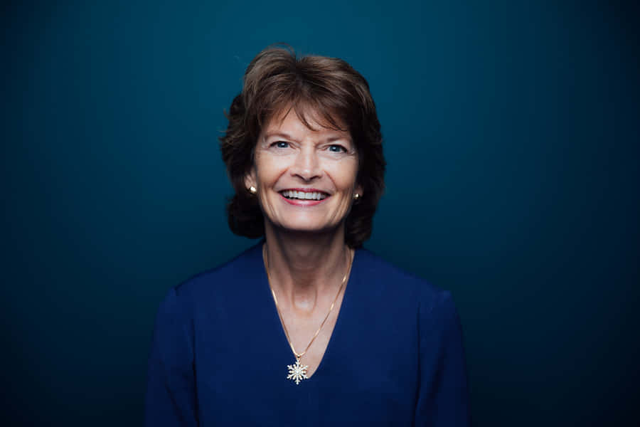 Senator Lisa Murkowski Smiling Against A Blue Aesthetic Background Wallpaper