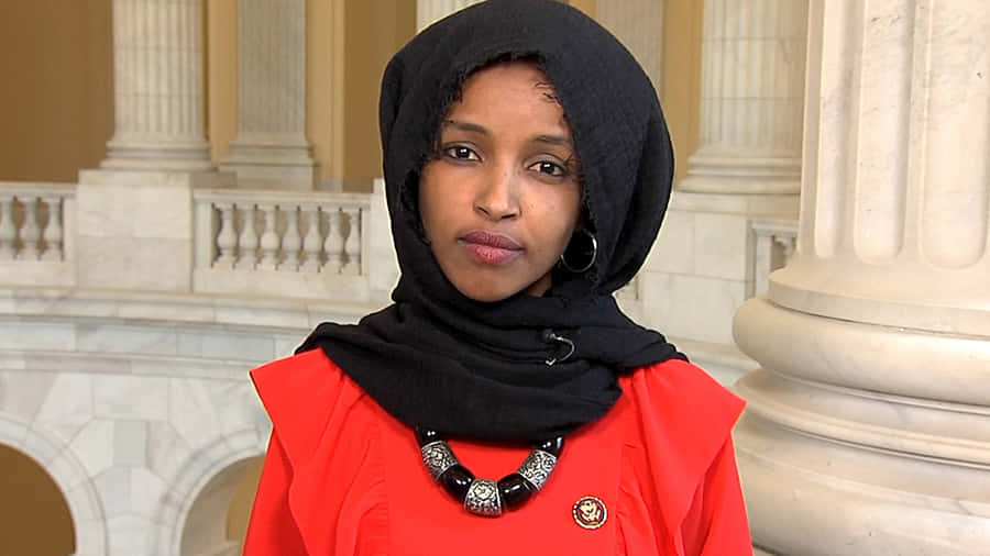 U.s. Representative Ilhan Omar Posing Elegantly In An Orange Dress Wallpaper