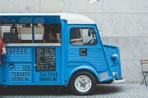 A Blue Food Truck With A Man Standing Next To It Wallpaper