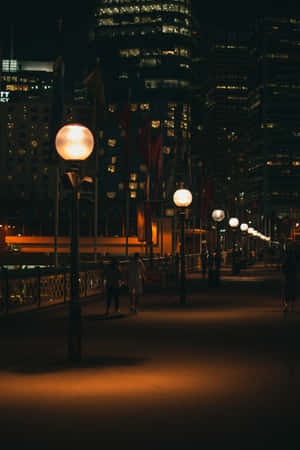 A City At Night With People Walking Along The Sidewalk Wallpaper