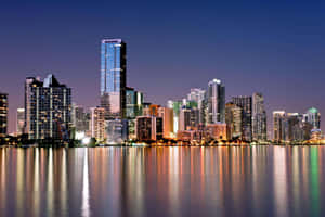 A City Skyline Is Reflected In The Water At Night Wallpaper