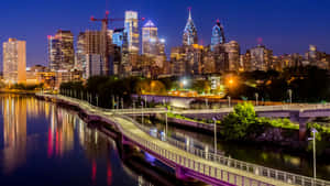 A City Skyline With A Bridge And River At Night Wallpaper