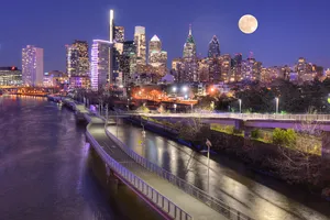 A City Skyline With A Full Moon Over A River Wallpaper