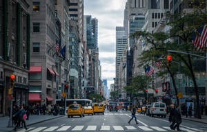 A City Street With Many People Walking And Crossing Wallpaper