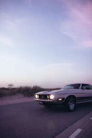 A Classic Car Driving Down The Road Wallpaper