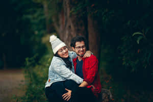 A Couple Sitting On A Log In The Woods Wallpaper