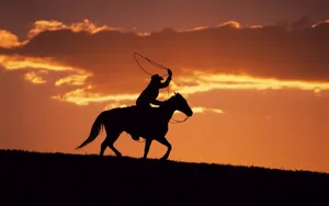 A Cowboy On A Horse Is Silhouetted At Sunset Wallpaper