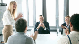 A Dynamic Team Meeting With Woman Leading The Presentation Wallpaper