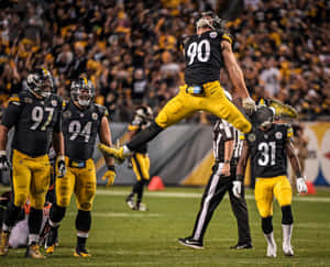 A Football Player Jumping In The Air While Others Watch Wallpaper