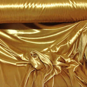 A Gold Satin Fabric Is Laying On A Table Wallpaper