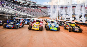 A Group Of Dirt Track Cars Driving In A Stadium Wallpaper