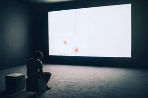 A Lonely Reflection: Man Sitting Alone In Theater Room Wallpaper