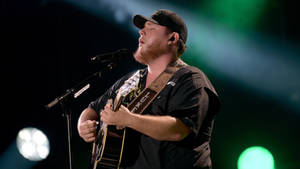 A Man In A Black Hat Singing Into A Microphone Wallpaper