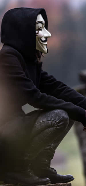 A Man In A Hoodie And Mask Sitting On A Rock Wallpaper