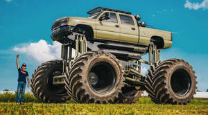 A Man Is Standing Next To A Large Truck With Large Tires Wallpaper