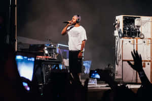 A Man On Stage With Microphones And A Crowd Wallpaper