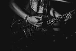 A Man Playing An Electric Guitar In The Dark Wallpaper