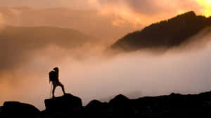 A Man Standing On Top Of Rocks In The Mountains At Sunset Wallpaper