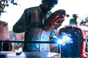 A Man Welding Metal On A Tractor Wallpaper