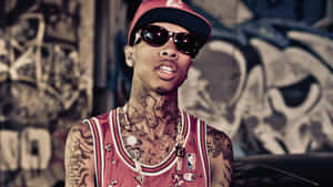 A Man With Tattoos And Sunglasses Standing In Front Of Graffiti Wallpaper