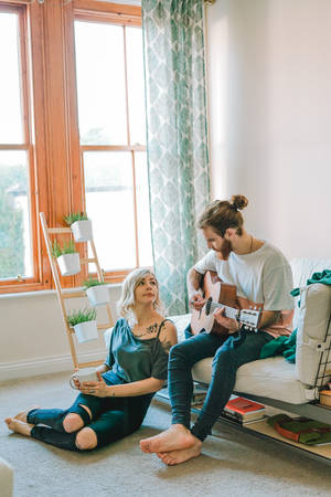 A Melody In Creation: An Artist's Hand Strumming A Classical Guitar Wallpaper