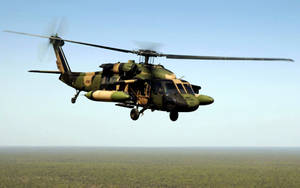 A Military Helicopter Flying Over A Forest Wallpaper