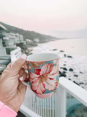 A Person Holding A Coffee Mug With A Flower On It Wallpaper