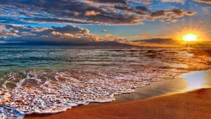 A Sunset Over A Sandy Beach With Waves Wallpaper