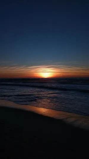 A Sunset Over The Ocean With A Sand Beach Wallpaper