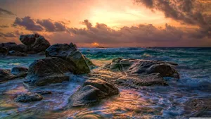 A Sunset Over The Ocean With Rocks And Water Wallpaper