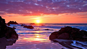 A Sunset With Rocks And Water Wallpaper