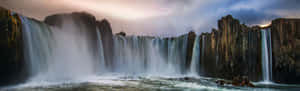 A Waterfall With A Cloudy Sky And Rocks Wallpaper